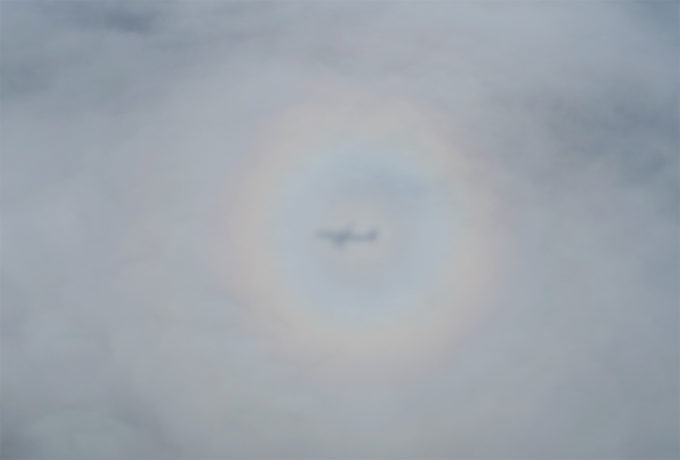 雲に飛行機の影と虹が